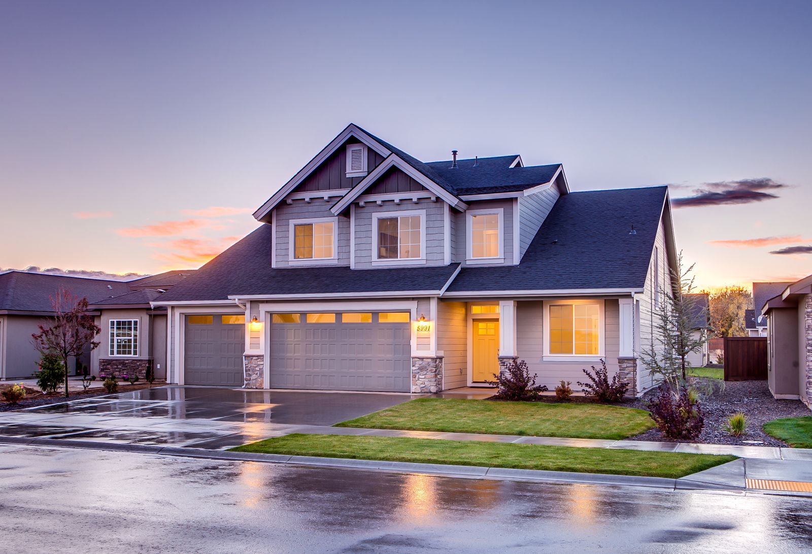 A two-storey suburban house with lit windows at dusk after rain