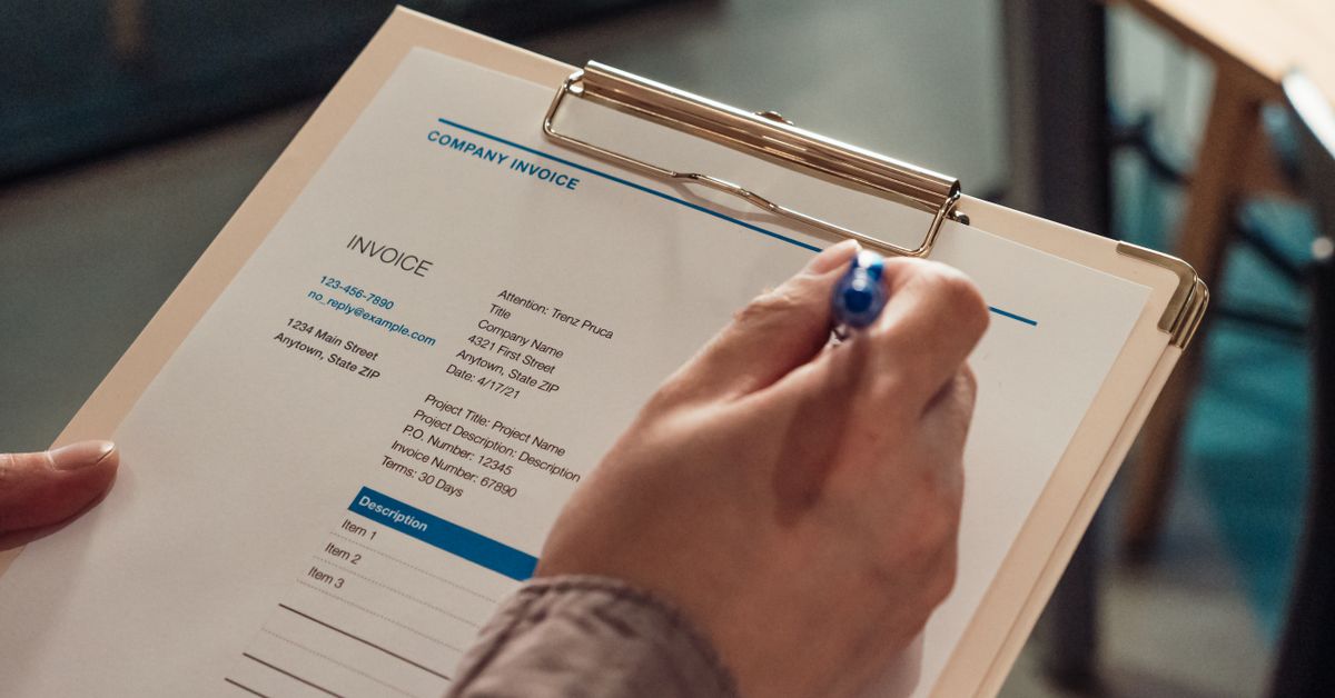 A hand filling out a company invoice form on a clipboard