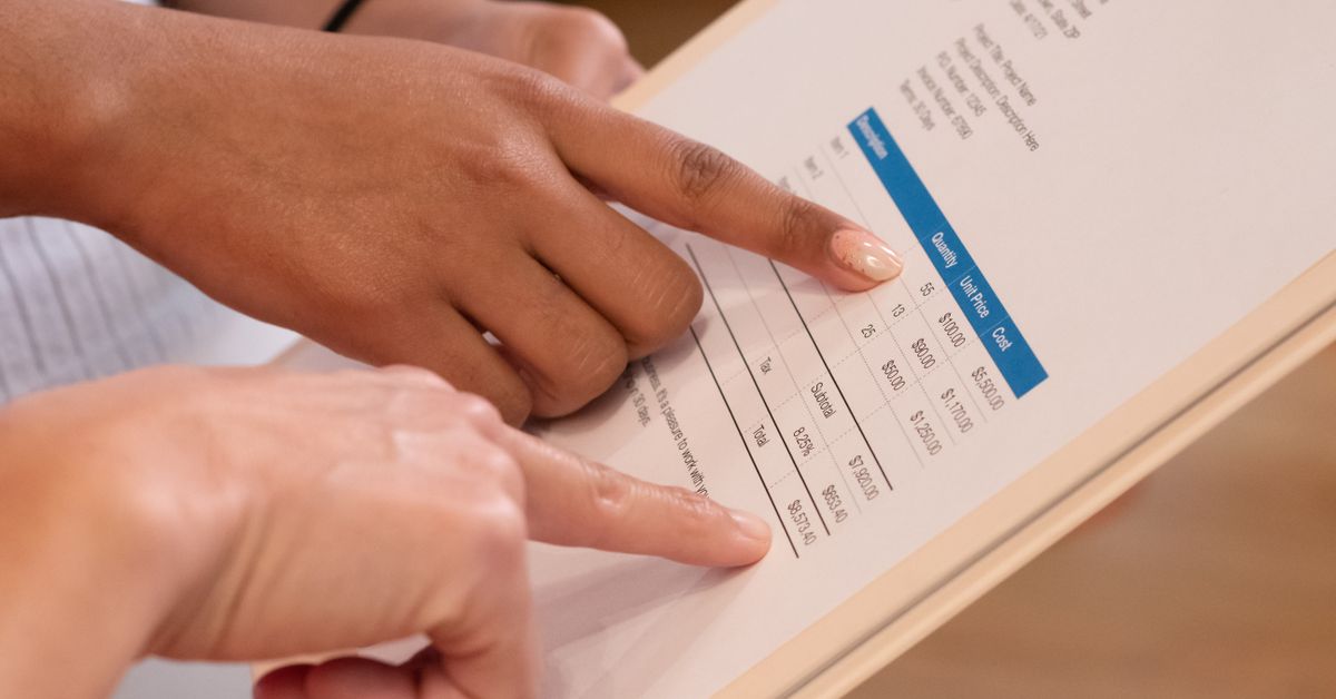 Two people reviewing the totals and tax lines on a printed invoice